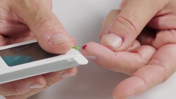 Prozess der Blutentnahme von einem Finger auf einen Teststreifen zur Bestimmung des Blutzuckers, hält die Hand eines Mannes ein elektronisches Glukometer mit einem Monitor, Blut fließt aus dem Finger, Nahaufnahme - Filmmaterial, Video