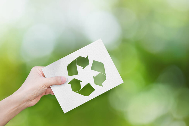 Milieuconcept. Hand houden van wit papier met recycle symbool op groene bokeh achtergrond. - Foto, afbeelding