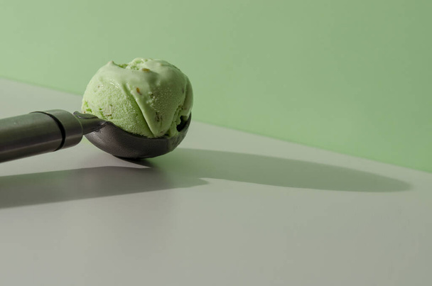 cuchara de helado con helado de pistacho sobre fondo verde pastel. Concepto de comida de moda - Foto, imagen