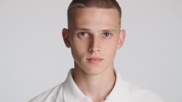 Ritratto di attraente ragazzo dagli occhi azzurri guardando con fiducia nella fotocamera su sfondo bianco - Filmati, video