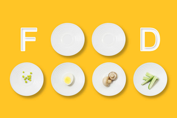 Healthy food minimalist flat lay. Food inscription and white plates with mushrooms, egg, peas and cucumbers on a yellow background. - Foto, Bild