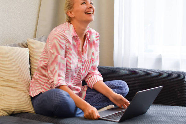 happy beautiful laughing woman with laptop laughs on the couch - Fotografie, Obrázek