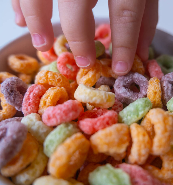 Bir çocuğun eliyle bir kasedeki renkli kahvaltı gevreğinin yakın görüntüsü - Fotoğraf, Görsel