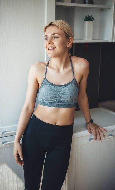 Caucasian blonde woman relaxing after doing fitness in sportswear at home and smile - Foto, imagen