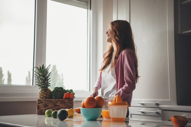 キッチンで笑顔しながら柑橘系の果物から新鮮なジュースを絞ると陽気な白人の生姜の女性 - 写真・画像