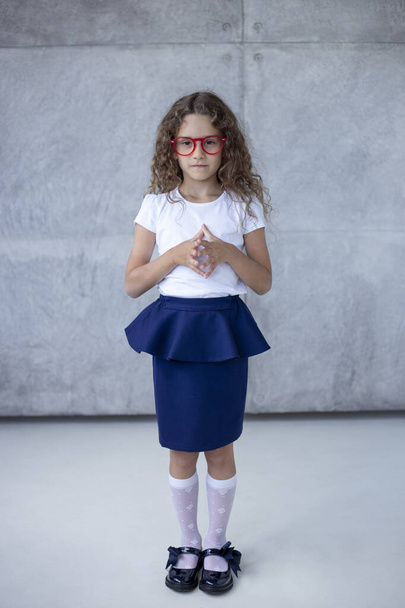 Petite fille, belle, en jupe, les mains sur la taille en lunettes rouges, isolée sur le fond concerté. - Photo, image