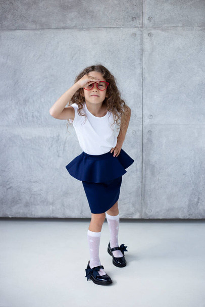 Ganzkörperbild eines hübschen kleinen Mädchens mit lockigem Haar, im Rock, mit roter Brille, isoliert auf dem Hintergrund. - Foto, Bild