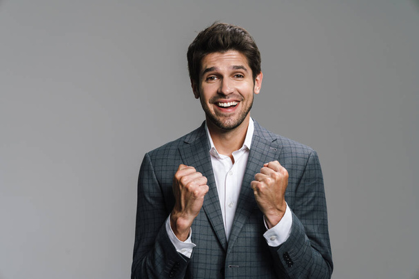 Photo of excited handsome businessman making winner gesture on camera isolated over grey wall - Foto, immagini