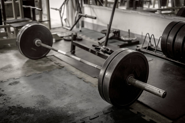 A rusty olympic size barbell loaded with plates on rubber matting. In position for deadlift. hardcore theme and setting. - Photo, Image