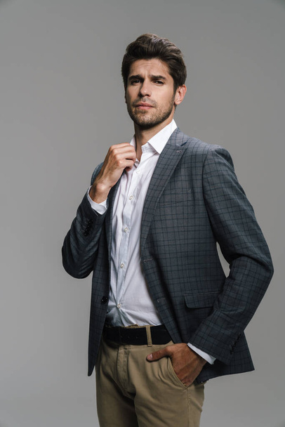 Photo of respectable confident businessman in jacket posing and looking at camera isolated over grey wall - Photo, Image