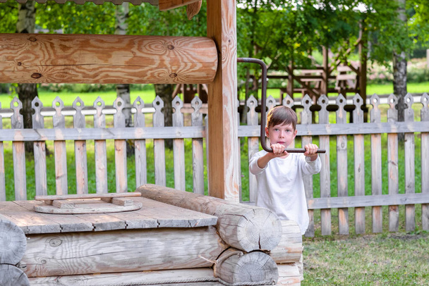 a boy gets water from a village well. child in the village. Russian traditions. Wood well - Photo, image