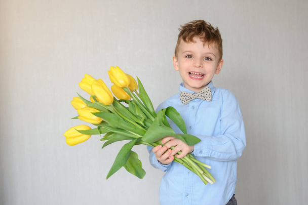 close up photo of a little boy with yellow tulips in his hands indoors - 写真・画像