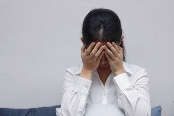 gestrest boos jong aziatisch vrouw met handen op gezicht zitten in woonkamer. - Foto, afbeelding