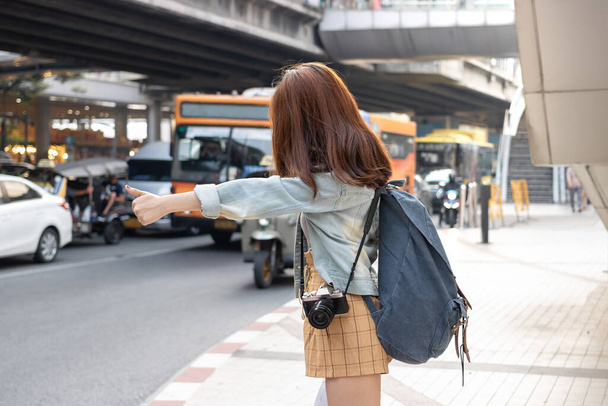Back view of young Asian travel girl hitchhiking on the road in city. Life is a journey concept. - Фото, изображение