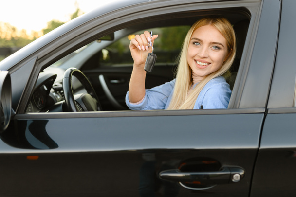 Happy woman with keys poses in car, lesson in driving school. Lady learns to drive vehicle. Drivers license education - Photo, Image