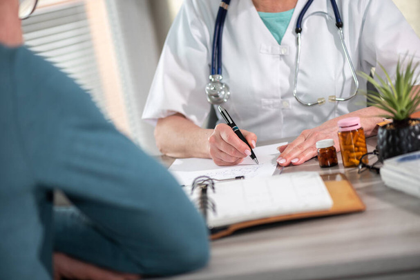 Kobieta lekarz wypisywanie recepty do jej pacjenta w gabinecie lekarskim - Zdjęcie, obraz