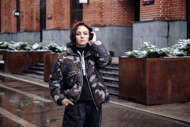 Stylish brunette woman in trendy apparel looking and enjoying winter in city. Outdoor lifestyle portrait of pretty young girl, wearing hipster swag grunge style on urban background. - Fotoğraf, Görsel