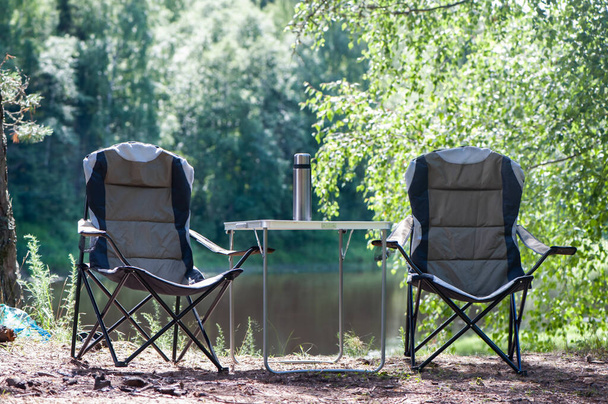 Tema de senderismo y turismo, un paisaje simbólico, dos sillas de camping vacías y mesa de picnic están en la hermosa playa, día soleado de verano
 - Foto, imagen