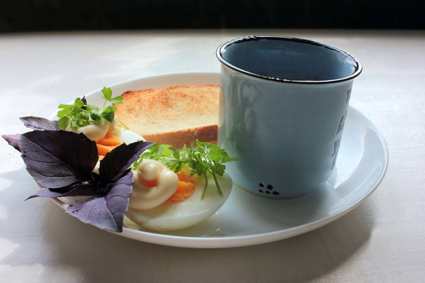 Œufs durs coupés en deux, persil, basilic vert, pain grillé blanc croustillant et tasse de café noir pour un petit déjeuner sain. Fond en bois blanc, ombre de plante. Vue du dessus - Photo, image