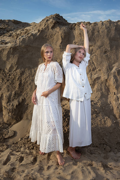 две привлекательные молодые сестры-близнецы позируют на песчаном карьере в элегантной белой одежде - Фото, изображение