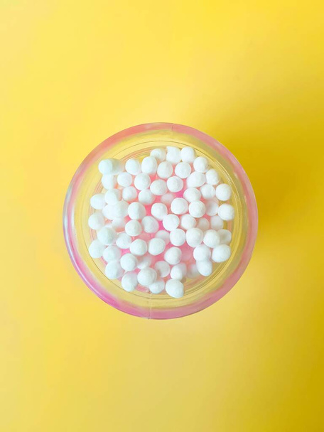 Ear sticks cotton pink plastic on a yellow background in a glass jar. Personal hygiene and care. Cosmetology and medicine. - Fotó, kép