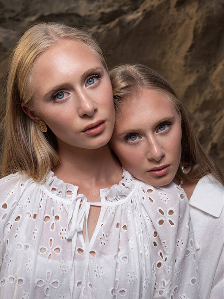 dos jóvenes rubias bonitas gemelas posando en la cantera de arena en ropa blanca elegante - Foto, Imagen