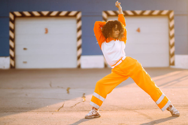 Afroamerikanisches Mädchen - Tänzerin, die bei Sonnenuntergang auf der Straße tanzt. Sport, Tanz und urbanes Kulturkonzept. Modischer Lebensstil. - Foto, Bild