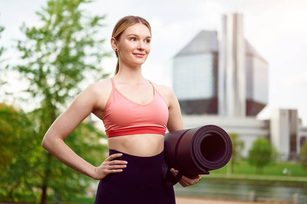 Mujer de fitness que usa ropa deportiva con alfombra de yoga al aire libre en el parque de verano - Foto, imagen