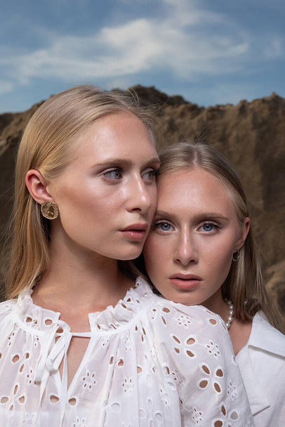 dwa młode blond ładne bliźniaki pozowanie w kamieniołomie piasku w eleganckich białych ubraniach - Zdjęcie, obraz