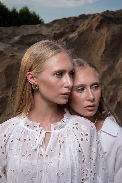 dwa młode blond ładne bliźniaki pozowanie w kamieniołomie piasku w eleganckich białych ubraniach - Zdjęcie, obraz