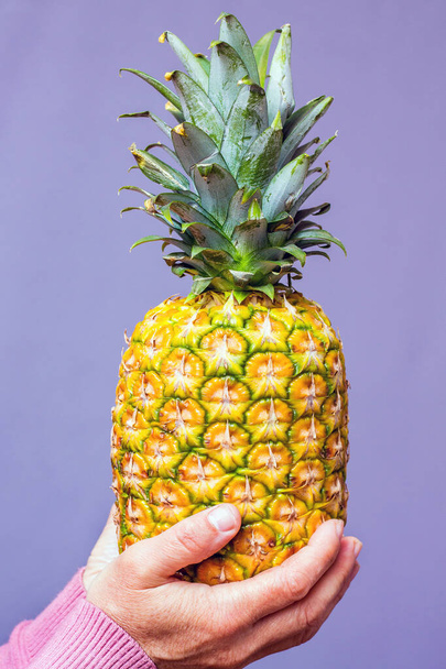 A woman holds a pineapple in the purple background - Fotografie, Obrázek