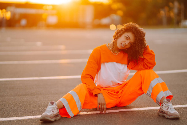 Stylish girl - dancer dancing in the street at sunset. Beautiful African  American woman with curly hair in an orange suit.  Sport, dancing and urban culture concept. - Foto, Imagem