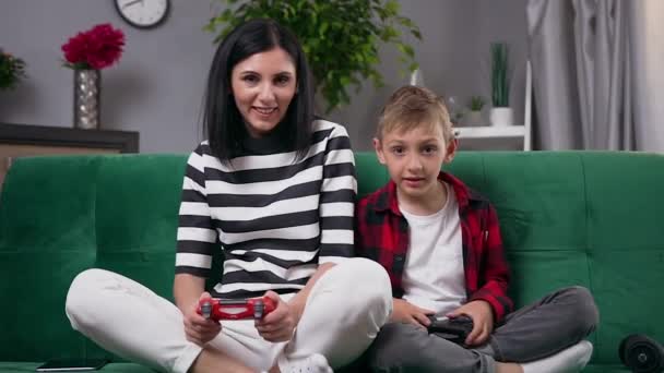 Sympatický šťastný moderní veselá mladá matka a 8-věk syn hraní videohry použití gamepady a baví společně, když matka vyhrává - Záběry, video