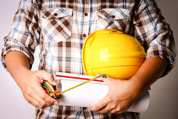 Der Bauamtsleiter trägt ein kariertes Hemd mit gelbem Schutzhelm und Baupapier. - Foto, Bild