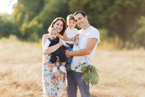 Family with children walking outdoors in summer field at sunset. Father, mother and two children sons having fun in summer field. People, family day and lifestyle concept - Photo, Image