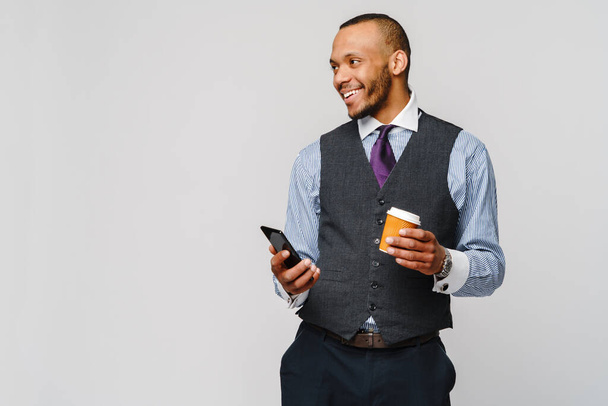 Young African-american Businessman holding Phone And Coffee to go over light grey background - Foto, Imagem