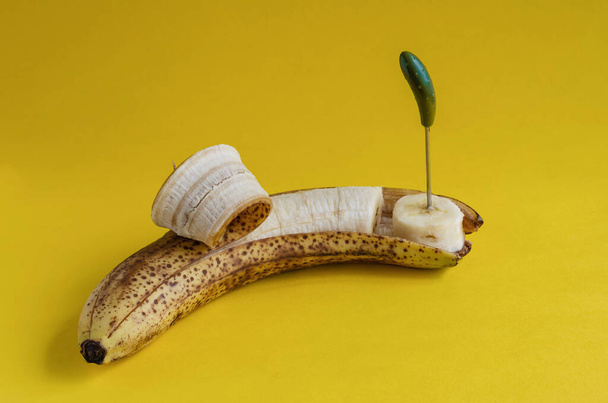 Перезрелый банан с частично очищенной кожей и канапе шампуров. Нарезанные сладкие фрукты на желтом фоне. Вид сбоку. Селективный фокус. - Фото, изображение