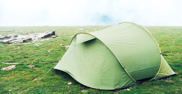 Tenda no deserto. Uma única tenda de acampamento verde em um prado gramado com nevoeiro na montanha. Trekking, camping, caminhadas e conceito de vida selvagem. Aventura ao ar livre real
. - Foto, Imagem