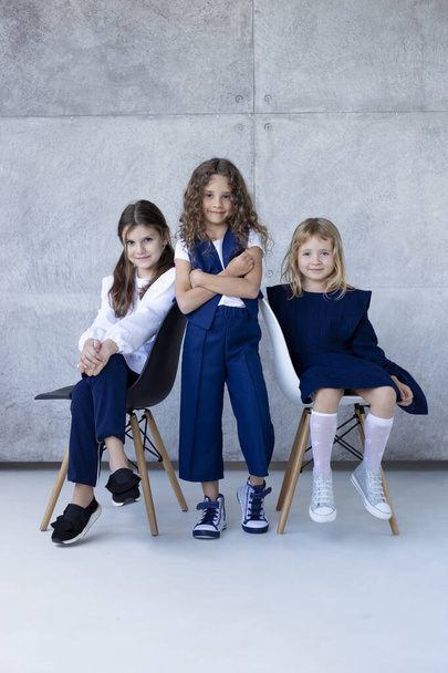 Ολόσωμο πορτραίτο τριών κοριτσιών μαθητών και προσχολικής ηλικίας, ντυμένων με σχολικές στολές, ποζάρουν στο στούντιο με υφάκι. Πίσω στο σχολείο.. - Φωτογραφία, εικόνα