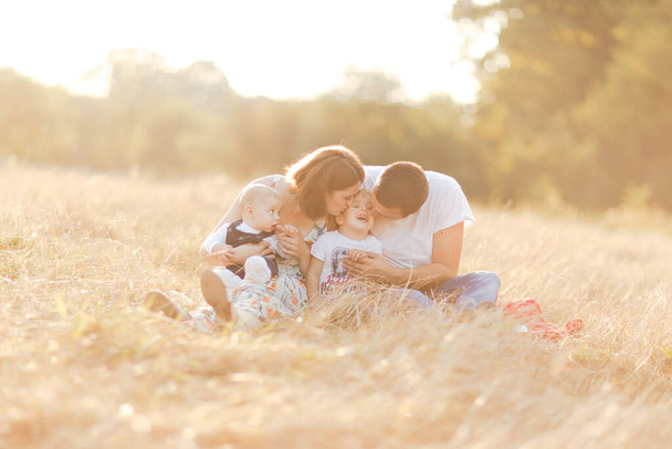 Family with children walking outdoors in summer field at sunset. Father, mother and two children sons having fun in summer field. People, family day and lifestyle concept - Foto, Imagen