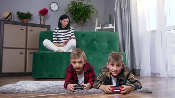 Close up of pretty smiling young woman sitting on couch and using i-pad while her two happy handsome carefree sons playing video game on the floor - Záběry, video
