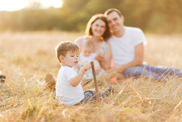 Family with children walking outdoors in summer field at sunset. Father, mother and two children sons having fun in summer field. People, family day and lifestyle concept - Фото, изображение