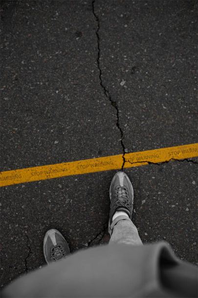 Μην διασχίζετε τη γραμμή άνθρωπος σε πάνινα παπούτσια στέκεται δίπλα σε μια κίτρινη γραμμή - Φωτογραφία, εικόνα