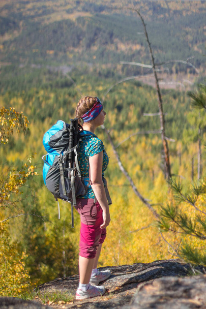 Red-haired girl standing with a backpack on a rock on a background of autumn forest - Foto, Bild