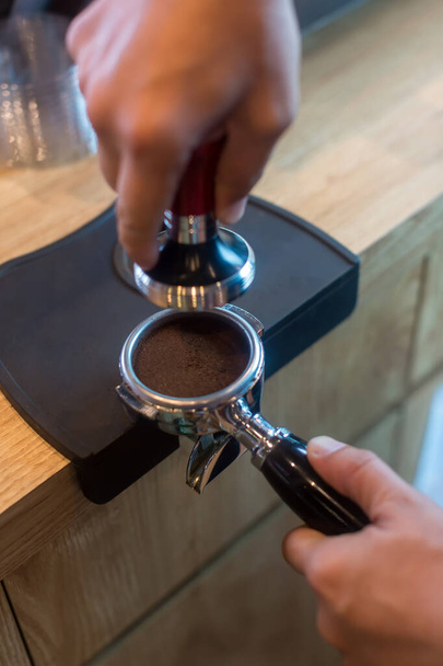 Barista pressing coffee in the machine holder. Coffee powder on coffee tamper. barista using tamper to press ground coffee into portafilter to make espresso hot drink. - Photo, Image