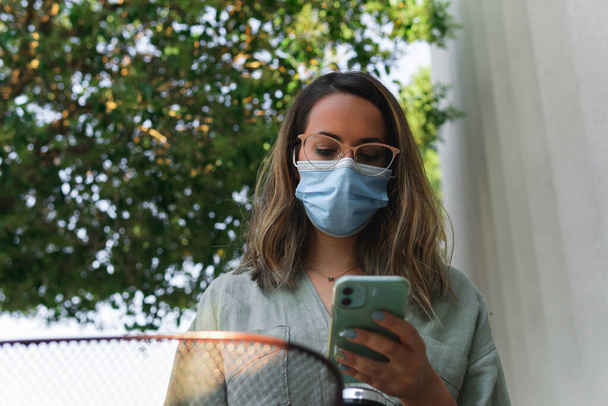 Young girl with glasses and face protection mask looking at her smartphone - Photo, Image