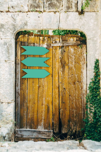 Taş duvarın oval girişinde metal işaretler olan eski ahşap bir kapı.. - Fotoğraf, Görsel