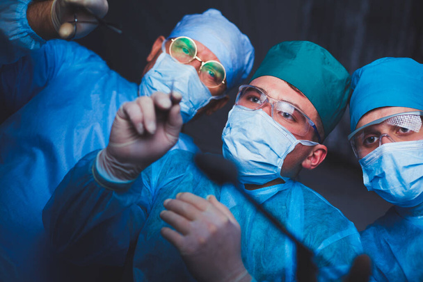 Group of surgeons at work in operating theater toned in blue. Medical team performing operation - Zdjęcie, obraz