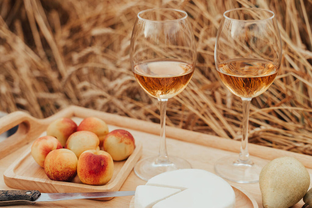 Letni wypoczynek na świeżym powietrzu. Piknik na polu pszenicy. Aperol, brzoskwinie, winogrona i ser - Zdjęcie, obraz