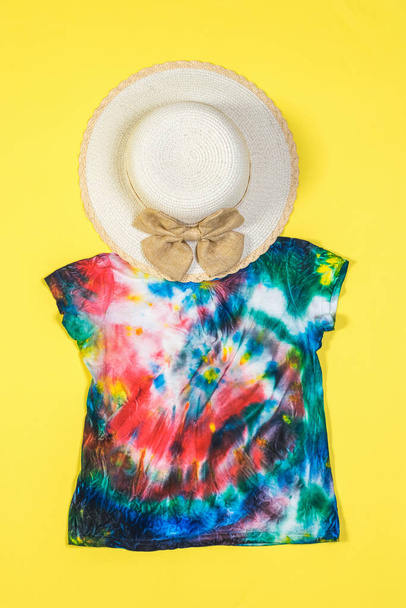 A large hat and tie dye t-shirt on a yellow background. Flat lay. - Photo, Image
